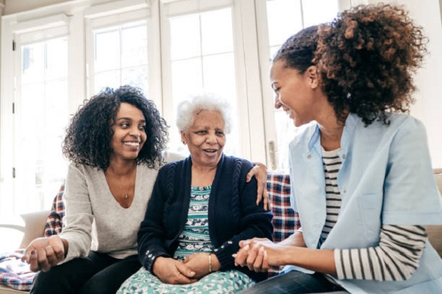 Photograph of cheerful caregiver with young lady and elderly woman